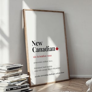 Könnte beinhalten: Ein gerahmter Druck mit den Worten "New Canadian" in Schwarz und einem roten Ahornblatt. Die Definition enthält Wörter wie "beharrlich" und "mutig". Ein Stapel Zeitschriften befindet sich vor dem Druck.