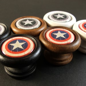 May include: Five wooden knobs with a red, white, and blue star design. The knobs are in different colors: black, brown, and white.
