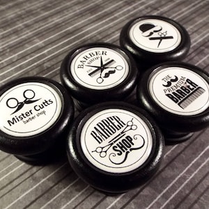 May include: Five black round wooden knobs with white labels featuring different barber shop designs. The labels include text such as "Mister Cutts barber shop", "Barber Shop", "The Premium Barber", and images of scissors, razors, and moustaches.