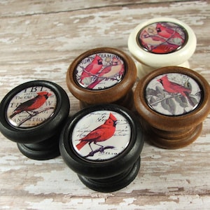 May include: Four wooden cabinet knobs with red cardinal bird designs. The knobs are in black, white, and brown finishes. The designs feature cardinals on branches with text in the background.