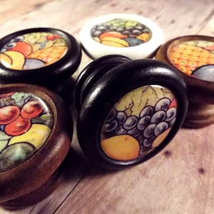 May include: Five different fruit themed cabinet knobs. The knobs are made of wood and have a round shape. The fruit designs include cherries, grapes, pineapple, and a mix of fruits.