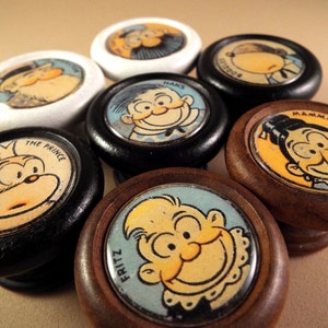 May include: Set of eight wooden knobs with cartoon faces. The knobs are painted in various colours and feature characters with names like "The Prince", "Fritz", "Mama", and "Rodger".