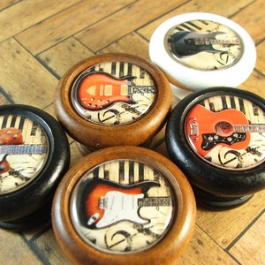 Peut inclure: Cinq boutons de cabinet à thème de guitare différents. Les boutons sont en bois et ont une finition noire, blanche ou brune. Chaque bouton présente un design de guitare différent avec des notes de musique et des touches de piano en arrière-plan.