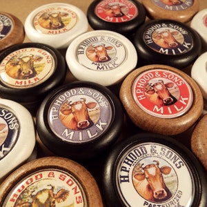 May include: A collection of 12 vintage-style milk bottle caps with a red, white, and blue color scheme. Each cap features a cow and the text "H.P. Hood & Sons" and "Milk".