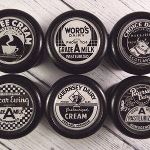 Peut inclure: Six bouchons de bouteille de lait noirs et blancs avec différents logos de laiteries. Les logos incluent "Coffee Cream", "Word's Dairy", "Choice Dairy", "Oscar Ewing", "Guernsey Dairy" et "Riverside Dairy".