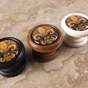 May include: Three decorative cabinet knobs featuring a fleur-de-lis design. The knobs are made of wood and have a black, white, and brown finish.