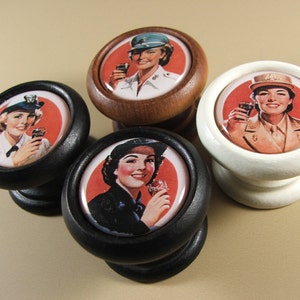 May include: Four round wooden knobs with a red, white and black background. Each knob features a woman in uniform holding a glass of Coca-Cola. The text "Coca-Cola" is visible on the glass.