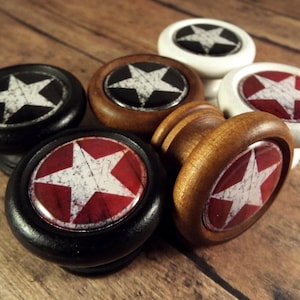 May include: Five wooden drawer knobs with a distressed white star on a red, black, or white background. The knobs are round and have a smooth finish.