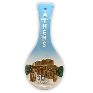 May include: A blue ceramic spoon rest with a 3D image of the Acropolis in Athens, Greece. The spoon rest has the word "ATHENS" written vertically on the handle and the word "GREECE" written below the image.