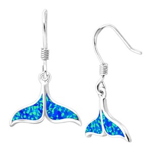 May include: A pair of silver-colored earrings featuring a whale tail design. The tails are filled with a blue and green opal-like material. The earrings have a hook closure.