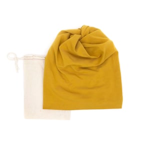 Pu&ograve; includere: Un berretto giallo senape e una borsa in lino naturale con coulisse. Il berretto &egrave; realizzato in un tessuto morbido ed elastico e ha una cima annodata.