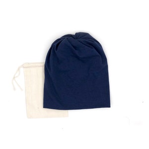 Pu&ograve; includere: Un berretto di stoffa blu navy con un nodo sulla cima, confezionato in una borsa di stoffa bianca con coulisse.