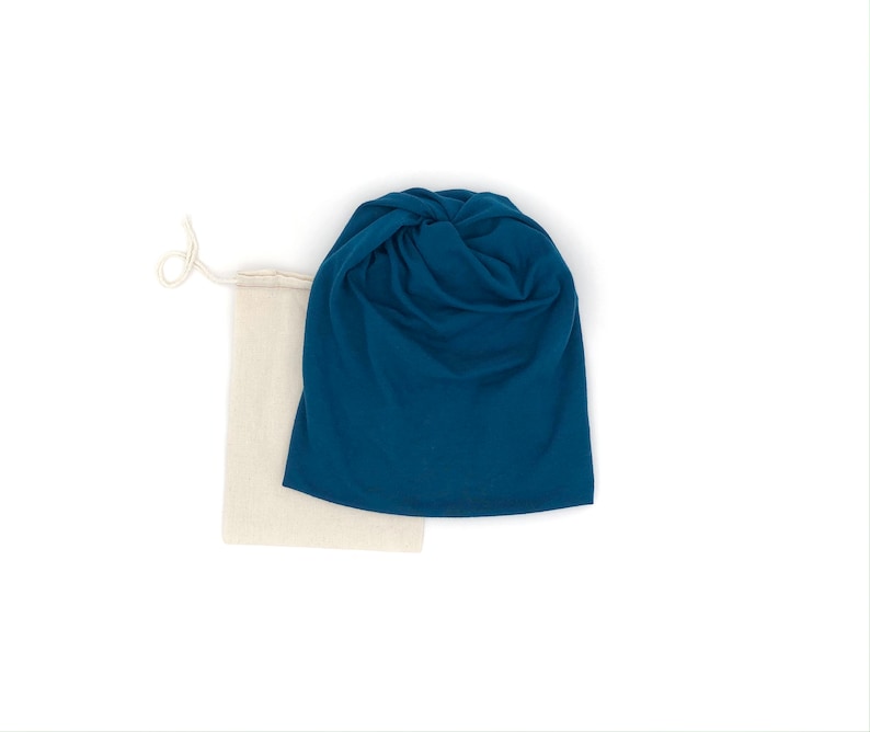 Pu&ograve; includere: Un berretto in tessuto blu turchese con un nodo sulla parte superiore, piegato e posizionato sopra una borsa con coulisse beige.