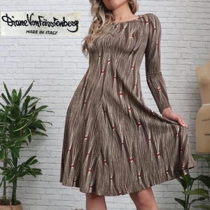 May include: A brown, long-sleeved dress with a unique pattern of vertical lines and red accents. The dress has a boat neckline and a flared skirt. The label "Diane Von Furstenberg MADE IN ITALY" is visible.