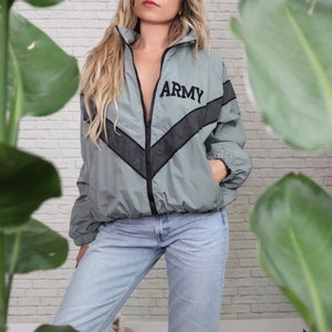 May include: A light grey windbreaker jacket with black chevron stripes and the word "ARMY" embroidered on the front. The jacket is zipped up and has a hood.