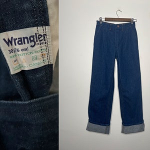 K&ouml;nnte beinhalten: Eine blaue Jeans aus Denim mit umgeschlagenem Saum. Die Jeans hat ein Etikett mit der Aufschrift "Wrangler 30/76 cm 100% Baumwolle/Coton Hergestellt in Kanada".