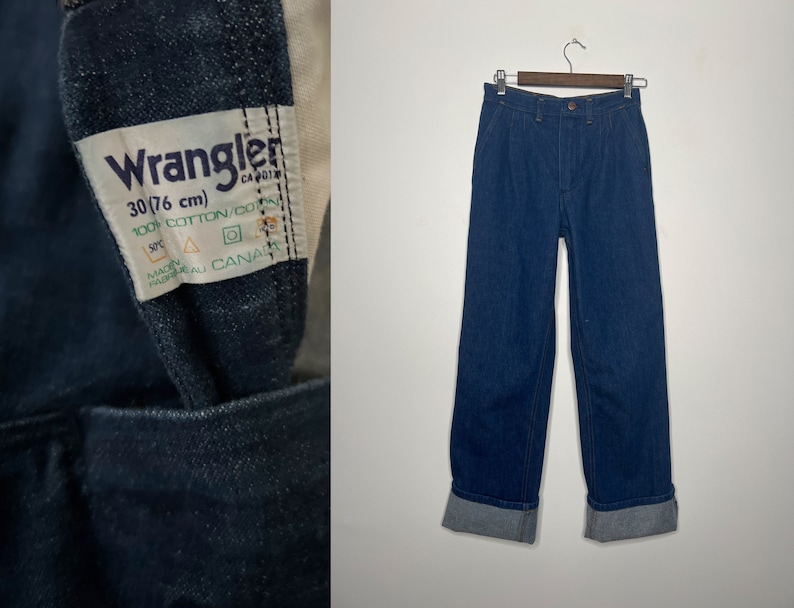 K&ouml;nnte beinhalten: Eine blaue Jeans aus Denim mit umgeschlagenem Saum. Die Jeans hat ein Etikett mit der Aufschrift "Wrangler 30/76 cm 100% Baumwolle/Coton Hergestellt in Kanada".