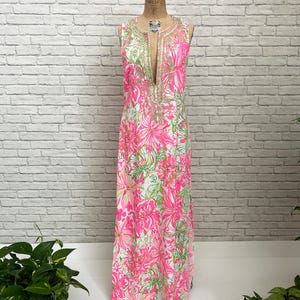 May include: A sleeveless floor-length maxi dress featuring a vibrant pink and lime green floral pattern on a white background. The garment has a deep V-neckline adorned with intricate gold-toned metallic embroidery and beadwork detailing.