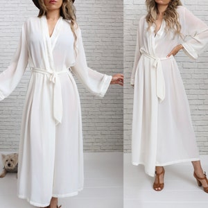 May include: A white sheer robe with long sleeves and a tie belt. The robe is made of a lightweight fabric and has a relaxed fit.