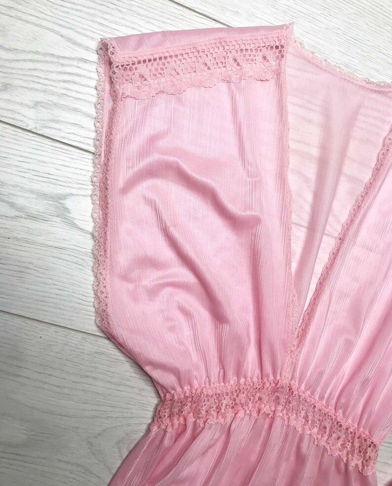 May include: A pink sheer dress with a V-neckline and lace trim. The dress has a gathered waist and a flowing skirt.