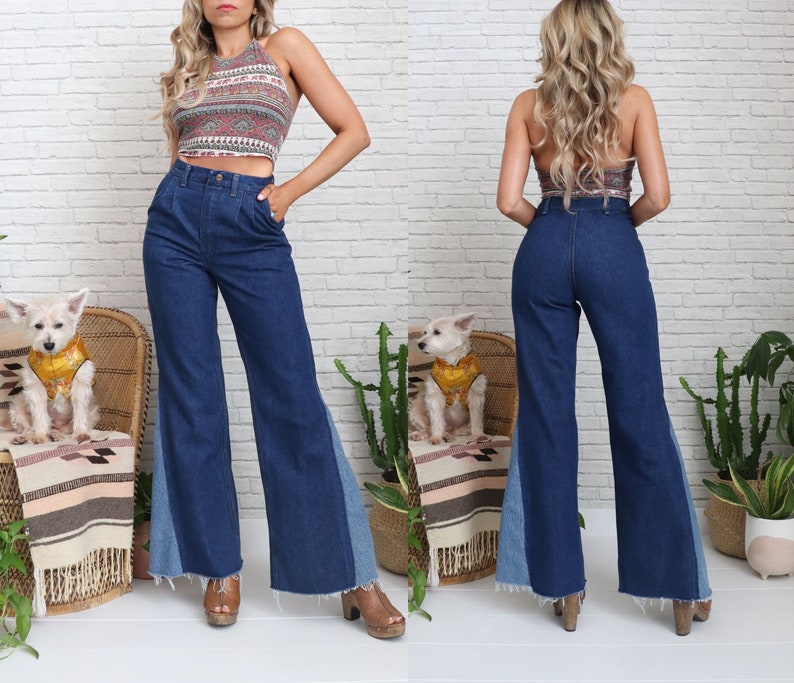 Pode incluir: Uma mulher vestindo uma cal&ccedil;a jeans azul de perna larga com um painel de jeans azul claro nas laterais. A cal&ccedil;a tem cintura alta e perna flare. A mulher tamb&eacute;m est&aacute; vestindo um top halter estampado.