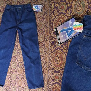 May include: Two pairs of blue denim jeans. One pair is folded and laid flat on a patterned fabric. The other pair is folded and laid flat on a patterned fabric. The jeans have a classic straight leg style. The jeans have a label that says "Wrangler" on it.