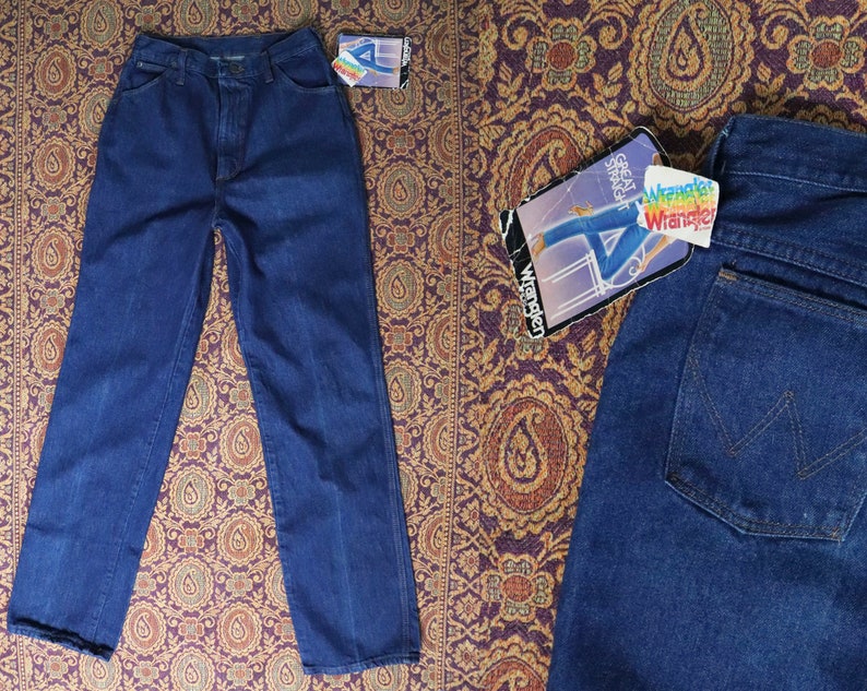 May include: Two pairs of blue denim jeans. One pair is folded and laid flat on a patterned fabric. The other pair is folded and laid flat on a patterned fabric. The jeans have a classic straight leg style. The jeans have a label that says "Wrangler" on it.