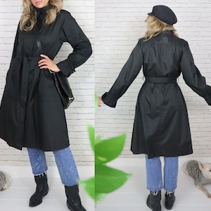 May include: A black raincoat with a belt and long sleeves. The raincoat has a high collar and a slightly flared skirt. The model is wearing blue jeans and cowboy boots.