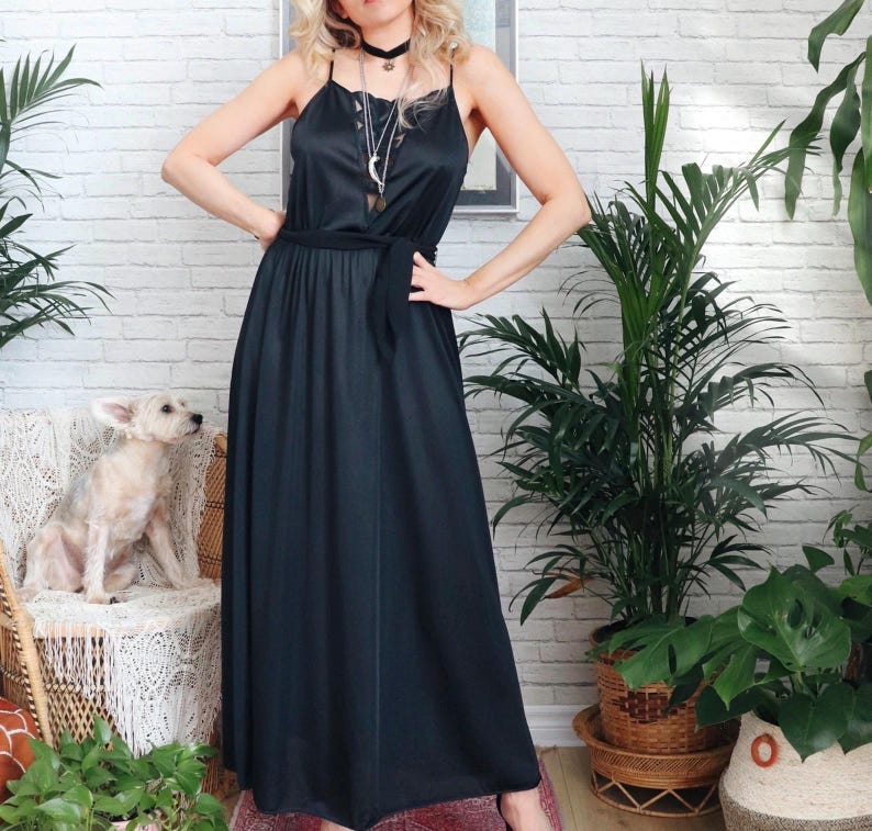 Puede incluir: Un vestido negro maxi con un cintur&oacute;n negro fino y tirantes finos. El vestido est&aacute; hecho de un material sedoso y tiene un corte holgado. La modelo lleva un collar plateado de varias capas con una gargantilla negra.