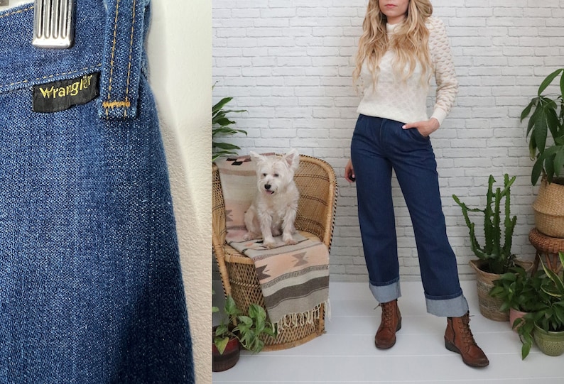 K&ouml;nnte beinhalten: Eine blaue Jeans aus Denim mit umgeschlagenem Saum und einem Wrangler-Etikett. Die Jeans wird von einer Person mit langen blonden Haaren und einem wei&szlig;en Pullover getragen. Die Person steht vor einer wei&szlig;en Backsteinwand.