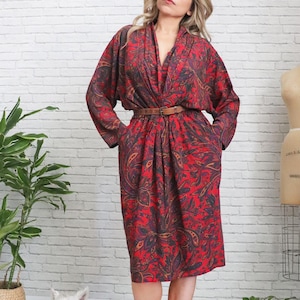 May include: A red paisley print dress with a brown leather belt. The dress has long sleeves and a V-neckline. The dress is knee-length and has pockets. The dress is made of a soft, flowing fabric.