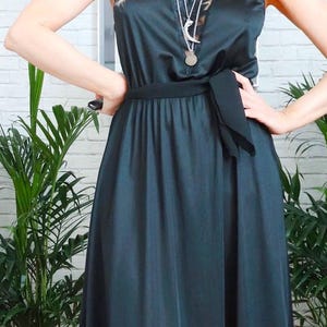 Puede incluir: Un vestido maxi de sat&eacute;n verde oscuro con una faja de sat&eacute;n negro anudada a la cintura. El vestido tiene un escote con ribete de encaje y la modelo lleva varios collares de plata.