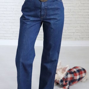 May include: A pair of dark blue denim jeans with a brown leather belt featuring a large metal buckle. The jeans have a high waist and a straight leg.