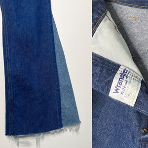 Pode incluir: Um par de cal&ccedil;as de ganga azuis de boca de sino com bainha desfiada. As cal&ccedil;as de ganga t&ecirc;m um painel de ganga azul contrastante na parte de tr&aacute;s de cada perna. As cal&ccedil;as de ganga t&ecirc;m uma etiqueta Wrangler com o texto "Wrangler 30/76 cm 100% algod&atilde;o" no bolso direito de tr&aacute;s.