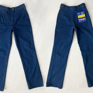 May include: A pair of dark blue denim jeans with a straight leg fit. The jeans have a button fly and belt loops. The jeans have a Wrangler brand label on the back pocket.