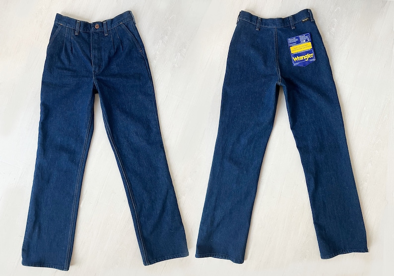 May include: A pair of dark blue denim jeans with a straight leg fit. The jeans have a button fly and belt loops. The jeans have a Wrangler brand label on the back pocket.