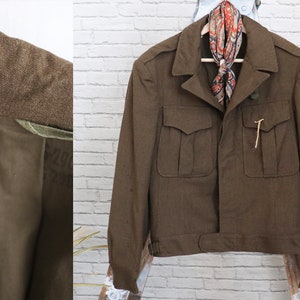 Pu&ograve; includere: Giacca marrone in stile militare con quattro tasche frontali e chiusura con bottoni. La giacca ha un colletto e un dettaglio in vita con cintura. Una sciarpa fantasia &egrave; appesa al colletto. La fodera interna &egrave; visibile.