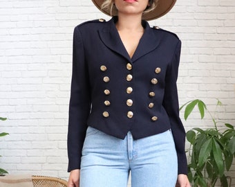 Könnte beinhalten: Ein marineblauer Blazer mit goldenen Knöpfen. Der Blazer hat eine verkürzte Länge und einen zweireihigen Verschluss.