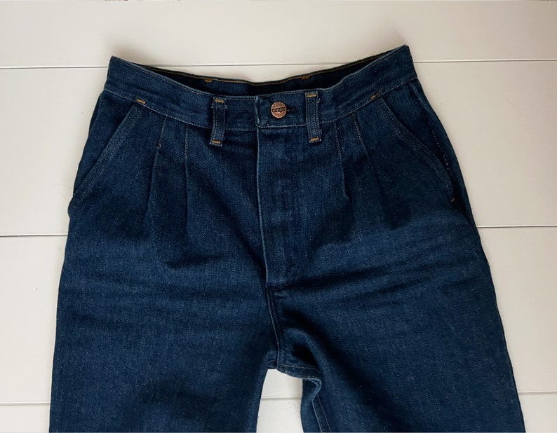 K&ouml;nnte beinhalten: Eine dunkelblaue Jeanshose mit Falten und einem Knopfverschluss.