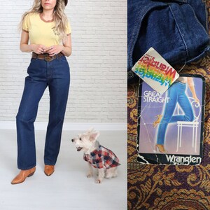 May include: A woman wearing a yellow t-shirt with a brown belt and blue jeans. She is standing next to a white dog wearing a red and black plaid shirt. The image also includes a close-up of a pair of blue jeans with a Wrangler tag that says "Great Straight".