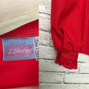 May include: A red long-sleeved blouse with a ruffled cuff and a JCPenney label. The blouse is made of a lightweight fabric.