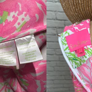 May include: A sleeveless dress featuring a vibrant pink, white, and green floral pattern. The interior includes a bright pink Lilly Pulitzer brand label and a white care tag stating 100% polyester, made in China, and Sugartown Worldwide, LLC.