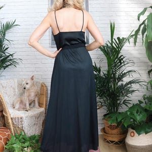 Puede incluir: Un vestido maxi negro con un corpi&ntilde;o de sat&eacute;n y una falda fluida. El vestido tiene tirantes finos y un cintur&oacute;n en la cintura.