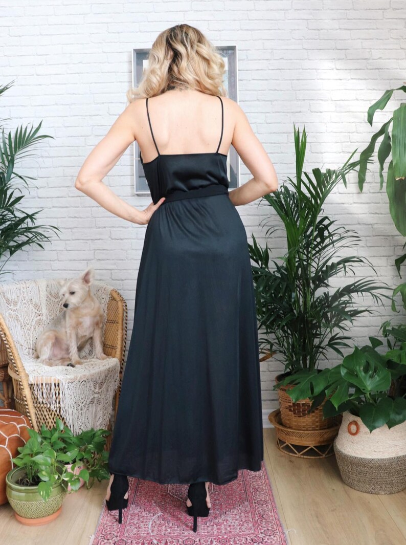 Puede incluir: Un vestido maxi negro con un corpi&ntilde;o de sat&eacute;n y una falda fluida. El vestido tiene tirantes finos y un cintur&oacute;n en la cintura.
