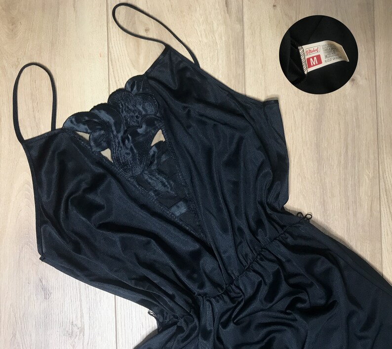 Puede incluir: Mono negro sin mangas con un dise&ntilde;o de encaje en el corpi&ntilde;o. El mono tiene una cintura con cord&oacute;n y una etiqueta de talla que dice "Ritchie" y "M".