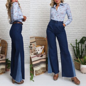 Pode incluir: Uma mulher est&aacute; vestindo uma blusa azul claro com estampa floral e uma cal&ccedil;a de sino azul jeans com um painel de jeans contrastante na lateral. Ela est&aacute; em p&eacute; na frente de uma parede de tijolo branco.