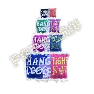 May include: A stack of colorful, knitted squares with the words "HANG TIGHT LOOSE KNIT" in white. The squares are in shades of blue, purple, green, pink, and red, with white trim. The text is in a bold, sans-serif font.