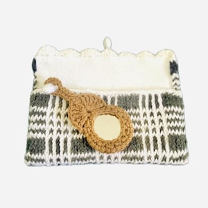 Puede incluir: Estuche de gafas de ganchillo hecho a mano con un adorno marrón en forma ovalada. El estuche presenta un patrón de cuadros blanco, gris y negro y un borde festoneado blanco.