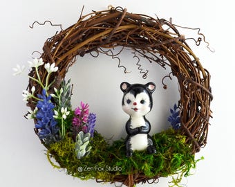 May include: A decorative wreath made of woven brown branches, adorned with colorful faux flowers and greenery. A ceramic skunk figurine with black and white markings sits in the center. The wreath includes the text "@Zen Fox Studio".