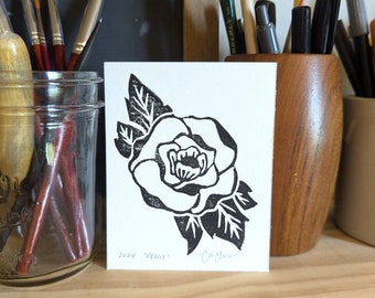May include: Black and white linocut print of a single rose with leaves. The print is titled "Peony" and signed "Carolyn".